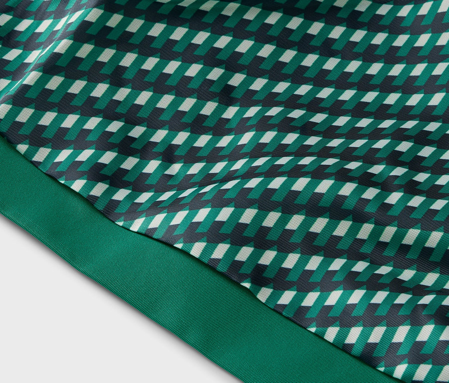 Detail látky s geometrickým vzorem v zelených, bílých a černých tónech a zelenou stuhou.