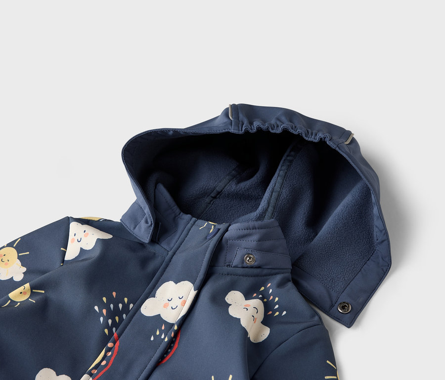 Detailní pohled na tmavě modrou bundu s kapucí, zdobenou motivy mraků a slunce.
