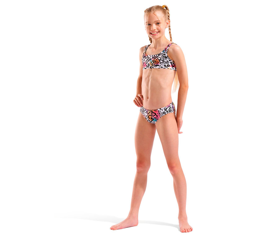 Dívka s blond copánky v bílých bikinách s barevným vzorem se usmívá.