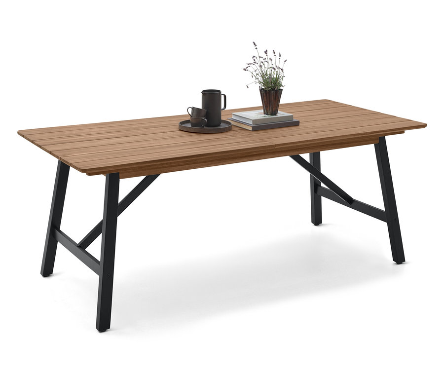 Na dřevěném stole s černými nohami stojí šálek, podšálek, kniha a rostlina.