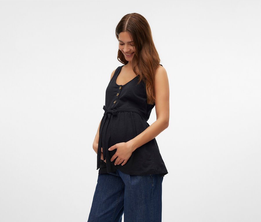 Žena drží si břicho a má na sobě černý top na kojení MAMALICIOUS »MLEVI LIA« a široké džíny.