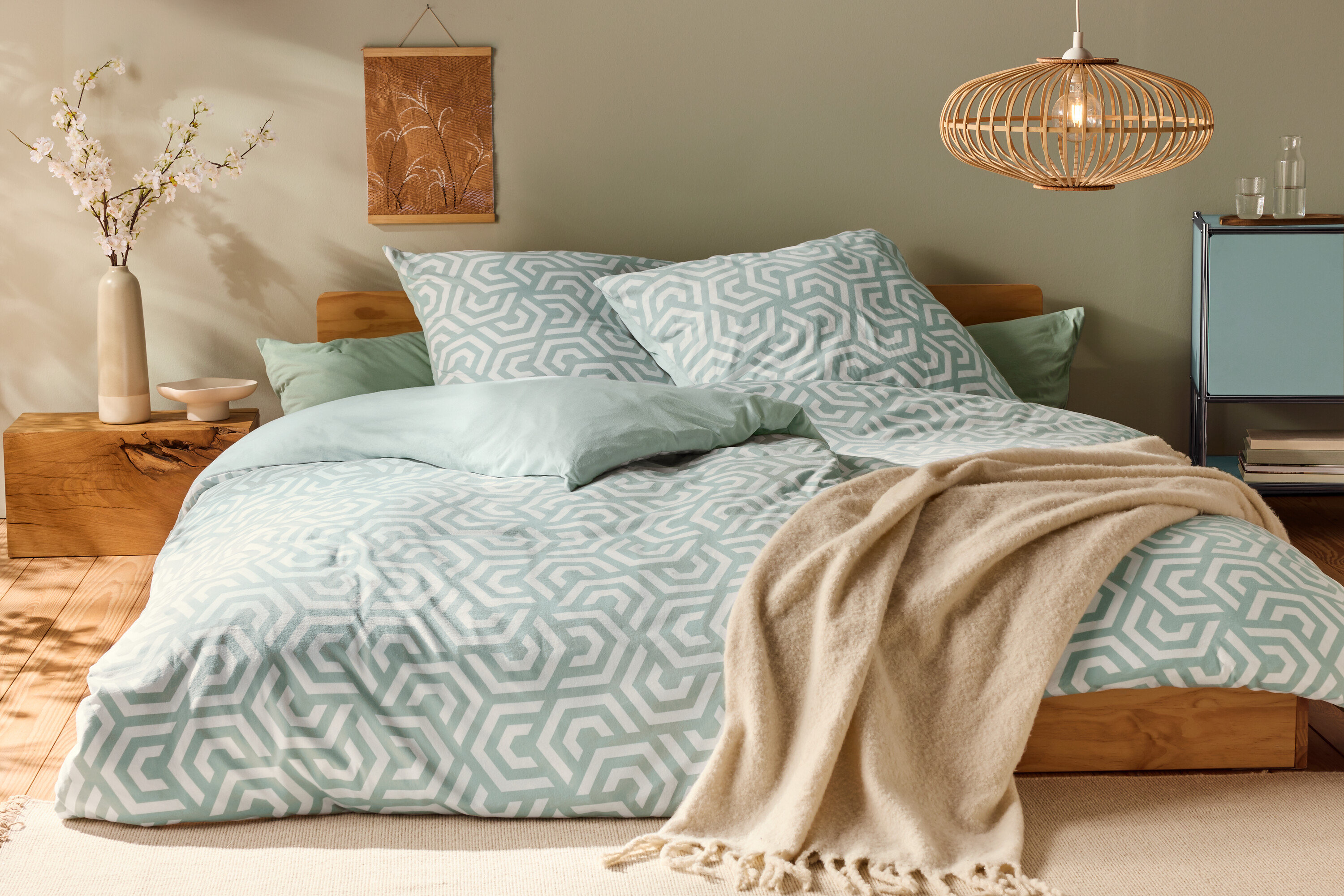 Postel s žerzejovým povlečením standardní velikosti s geometrickým vzorem a světle zelenými polštáři.