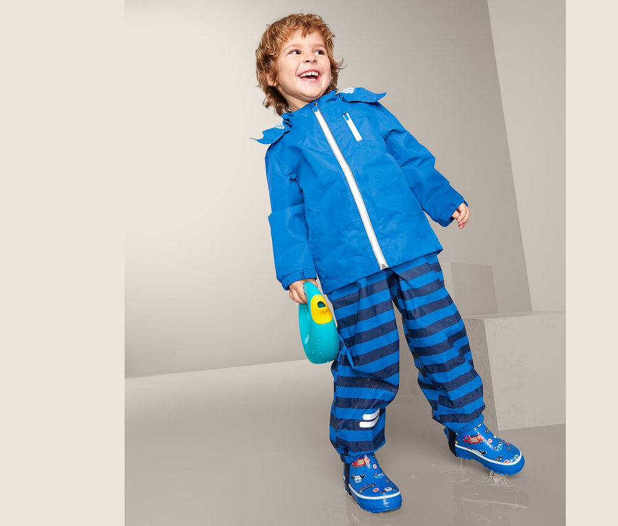 Chlapec má na sobě modrou bundu do deště, pruhované kalhoty a modré boty.