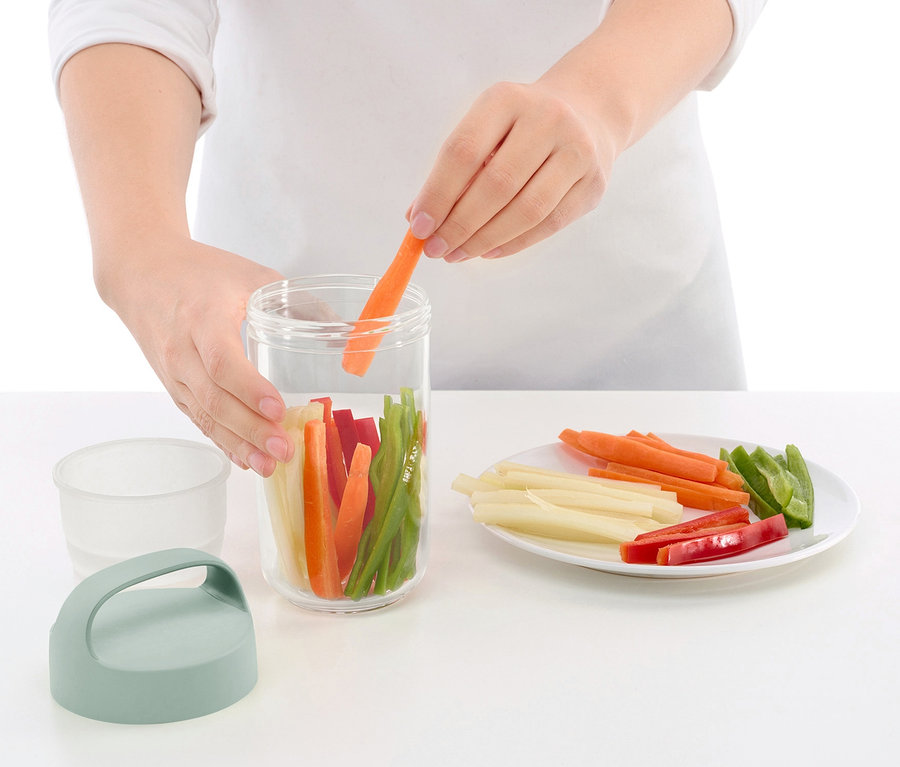 Osoba vkládá mrkev do cestovní dózy na oběd se zeleninou.