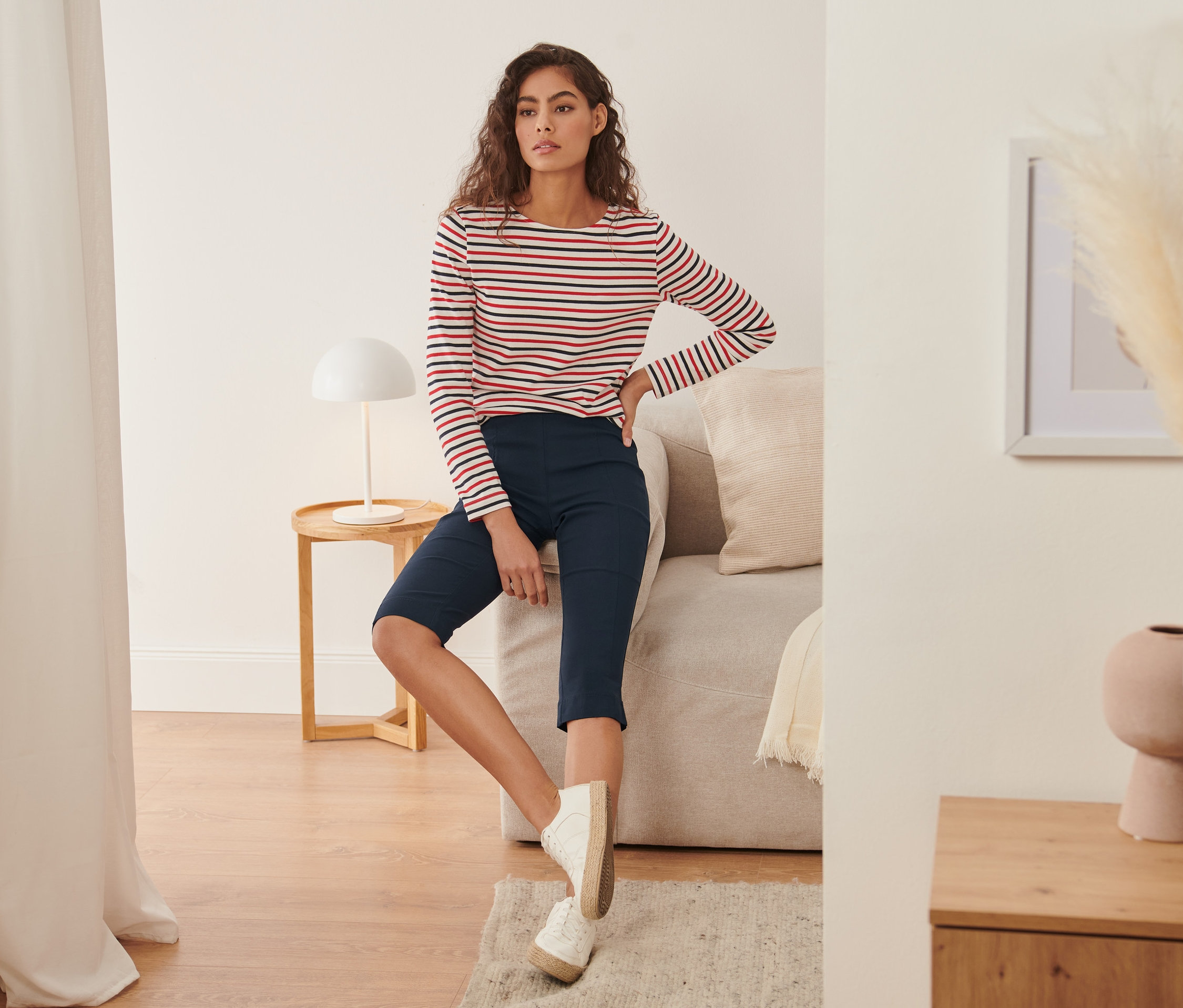 Žena sedí na pohovce a má na sobě 3/4 strečové kalhoty a pruhované tričko.