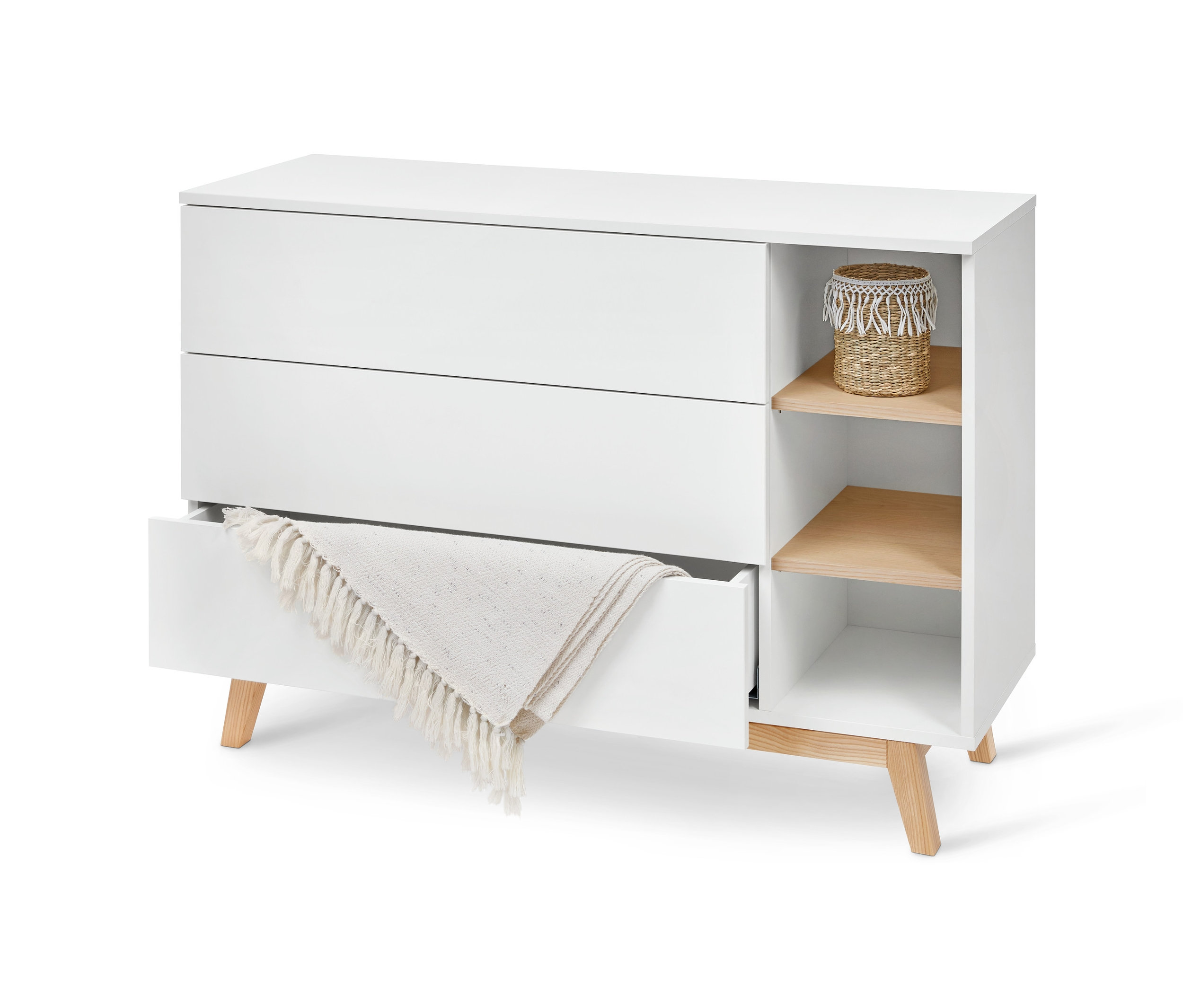 Bílá komoda se zásuvkami a přihrádkami. Jedna zásuvka je otevřená a je v ní deka.