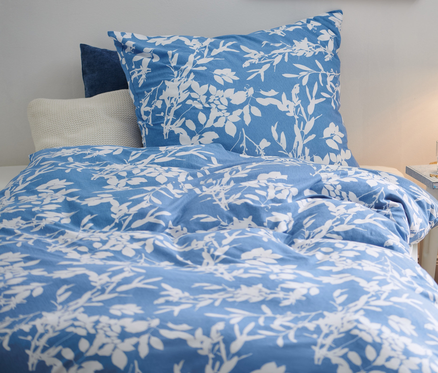 Ložní prádlo s květinovým vzorem na posteli vedle stolku s lampou.