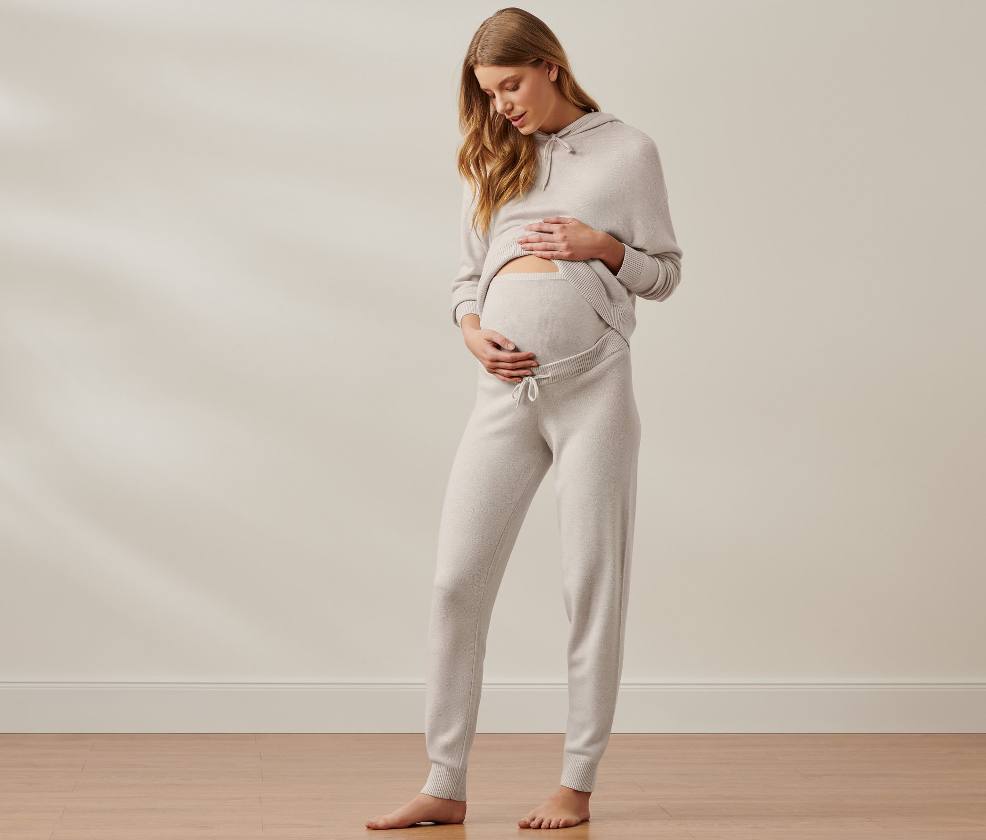Těhotná žena hladí břicho v pohodlné těhotenské soupravě.