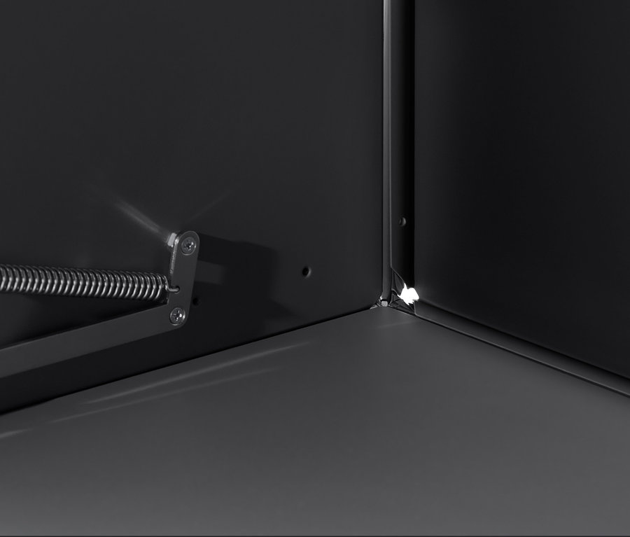 Detail vnitřku černé skříňky CN3 s výklopnými dvířky, zaměřený na roh a mechanismus otevírání.