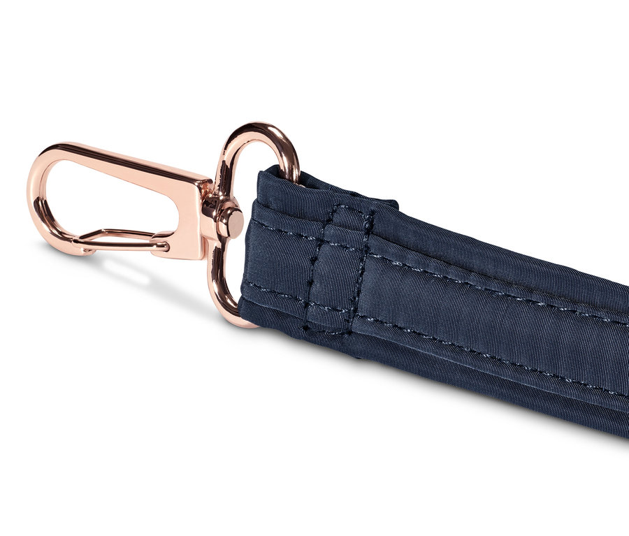 Detail modrého popruhu bezpečnostní tašky přes rameno s růžově zlatou karabinou.