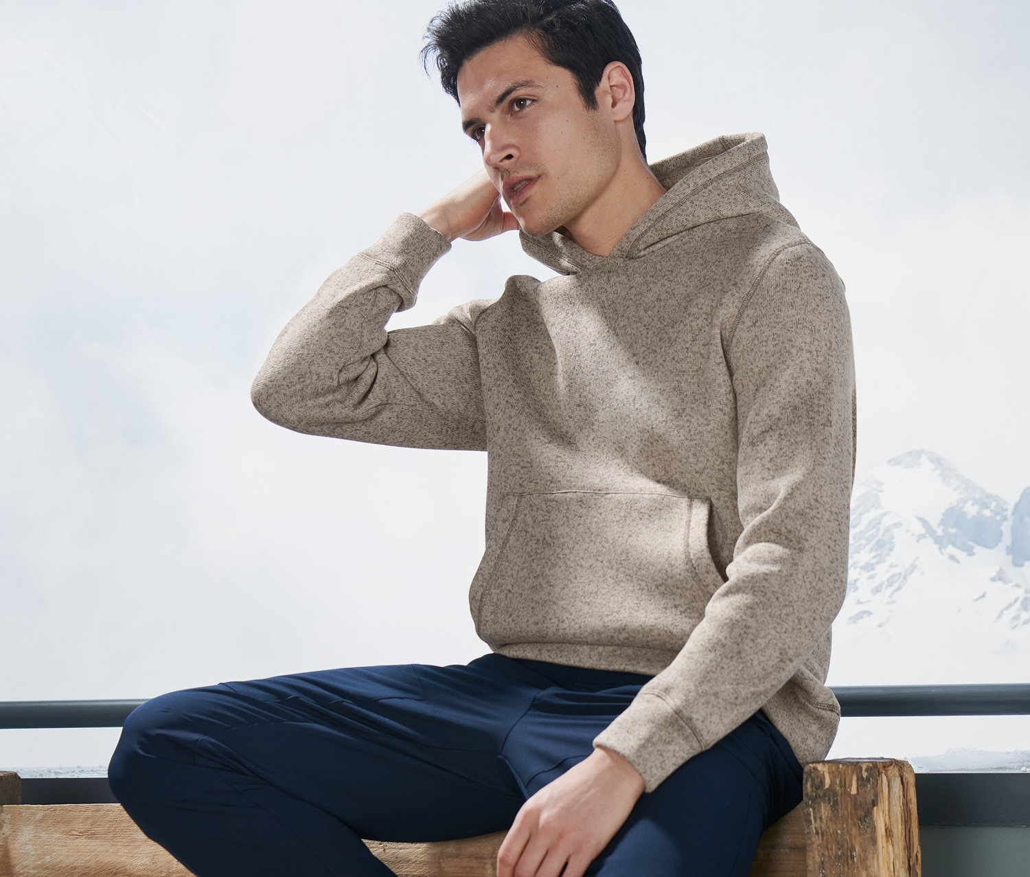 Muž sedí na lavičce a má na sobě pletenou fleecovou mikinu.