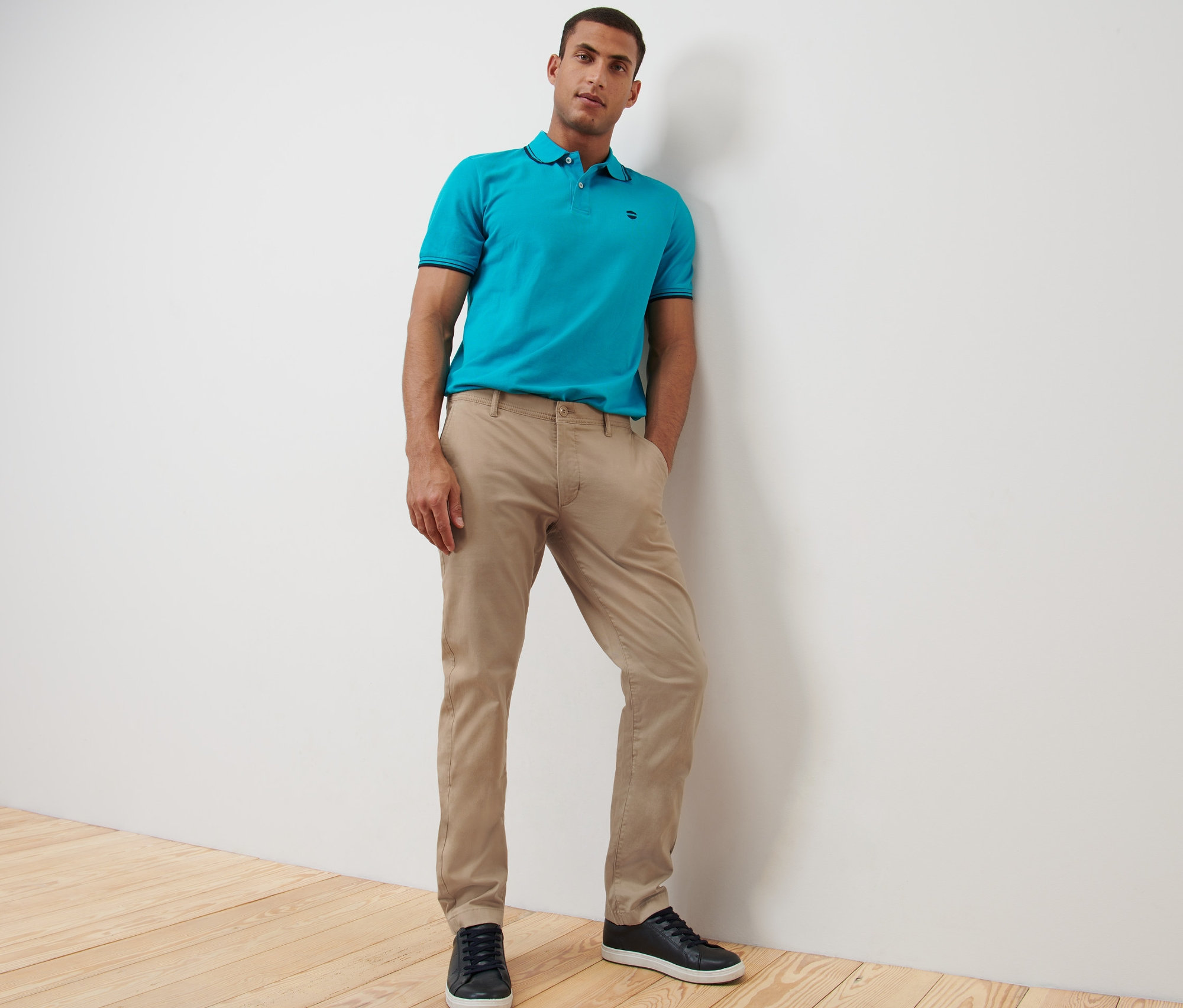 Muž pózuje v béžových kalhotách chino a modré polokošili.