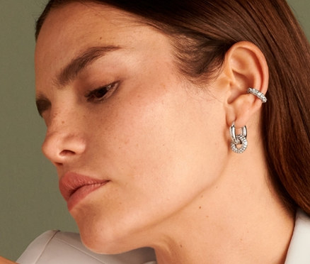 Žena sedí a má na sobě náušnici Ear cuff Sparkle Donut, prsten Sparkle Donut, kreolky Sparkle Donut a řetízek Sparkle Donut.