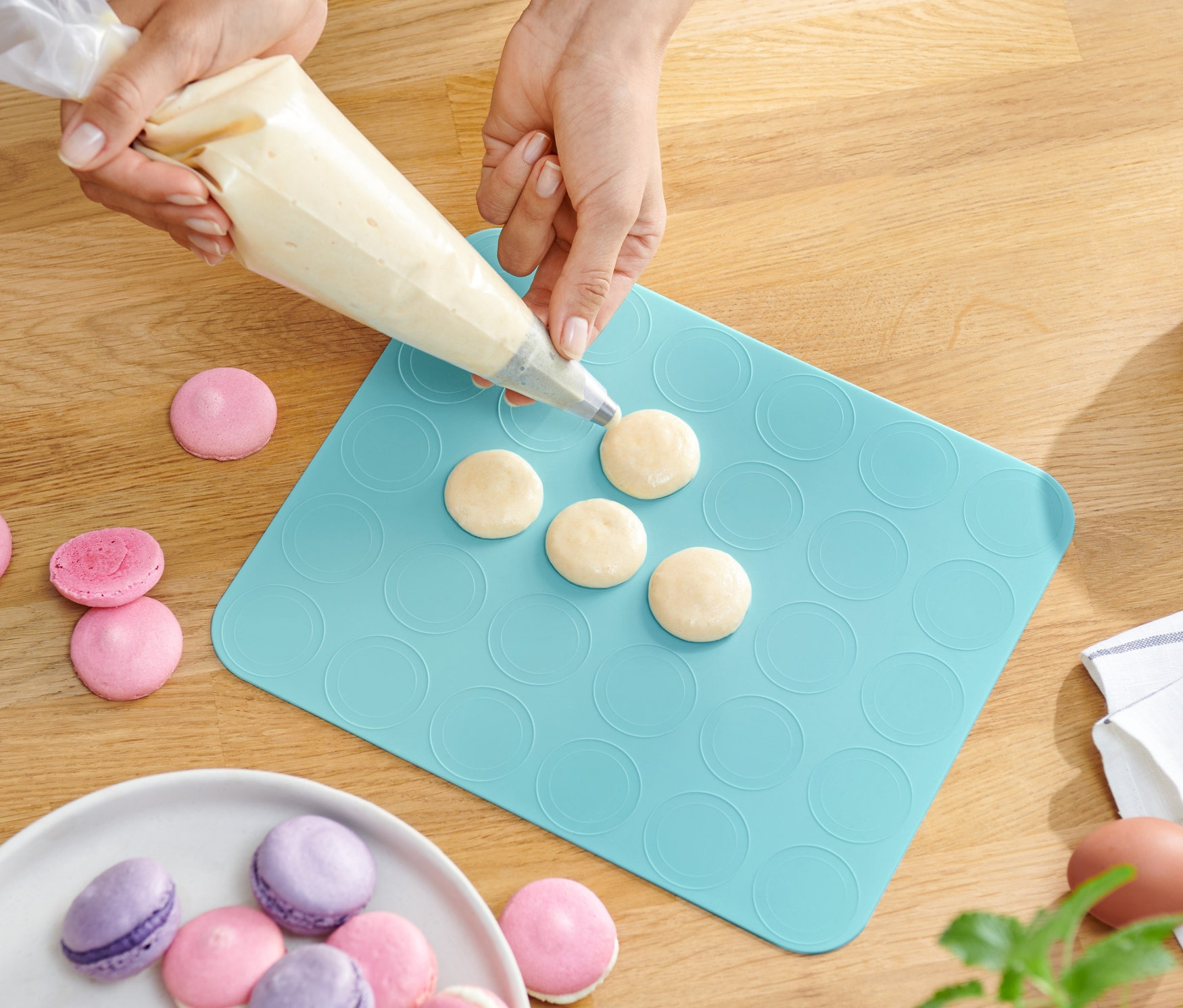 Osoba plní těsto na pečicí podložku na makronky. 