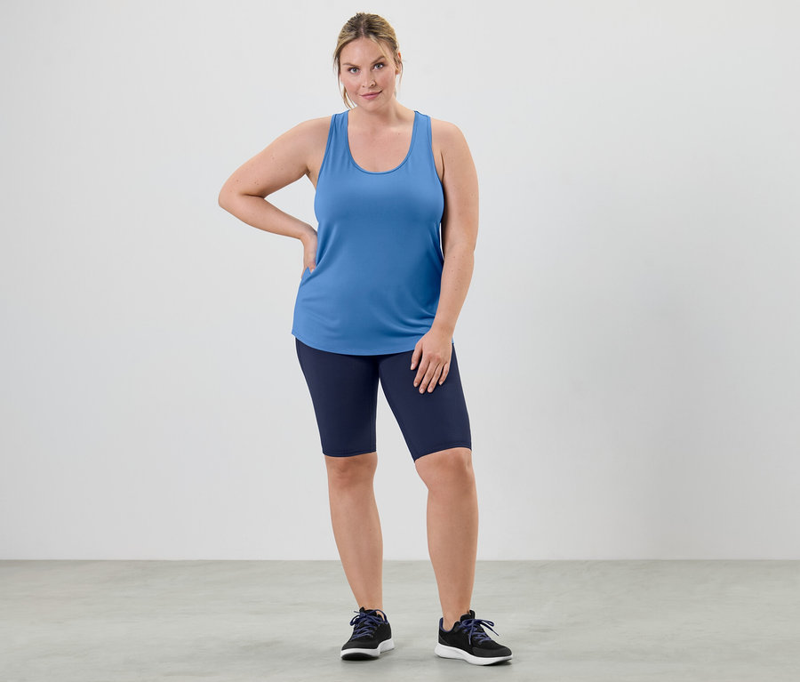 Žena pózuje ve funkčním topu nebesky modré barvy z dvoudílné sady a v cyklistických šortkách.