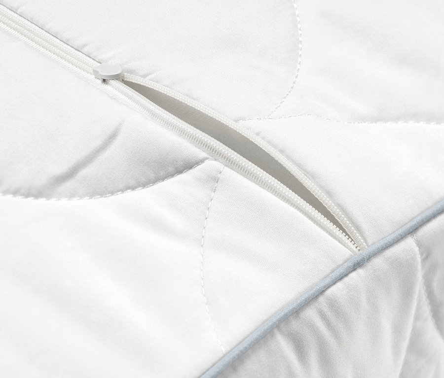Detail bílého prošívaného polštáře pro oporu krční páteře s částečně rozepnutým zipem.