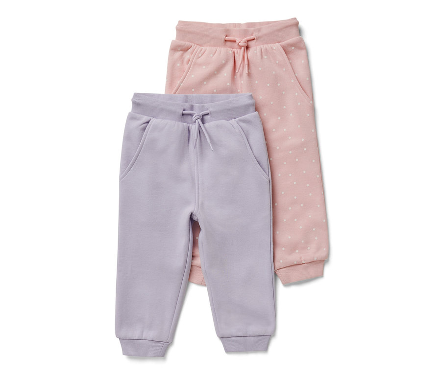 Dvoje dětské teplákové kalhoty: jedny světle fialové a jedny růžové s bílými puntíky.
