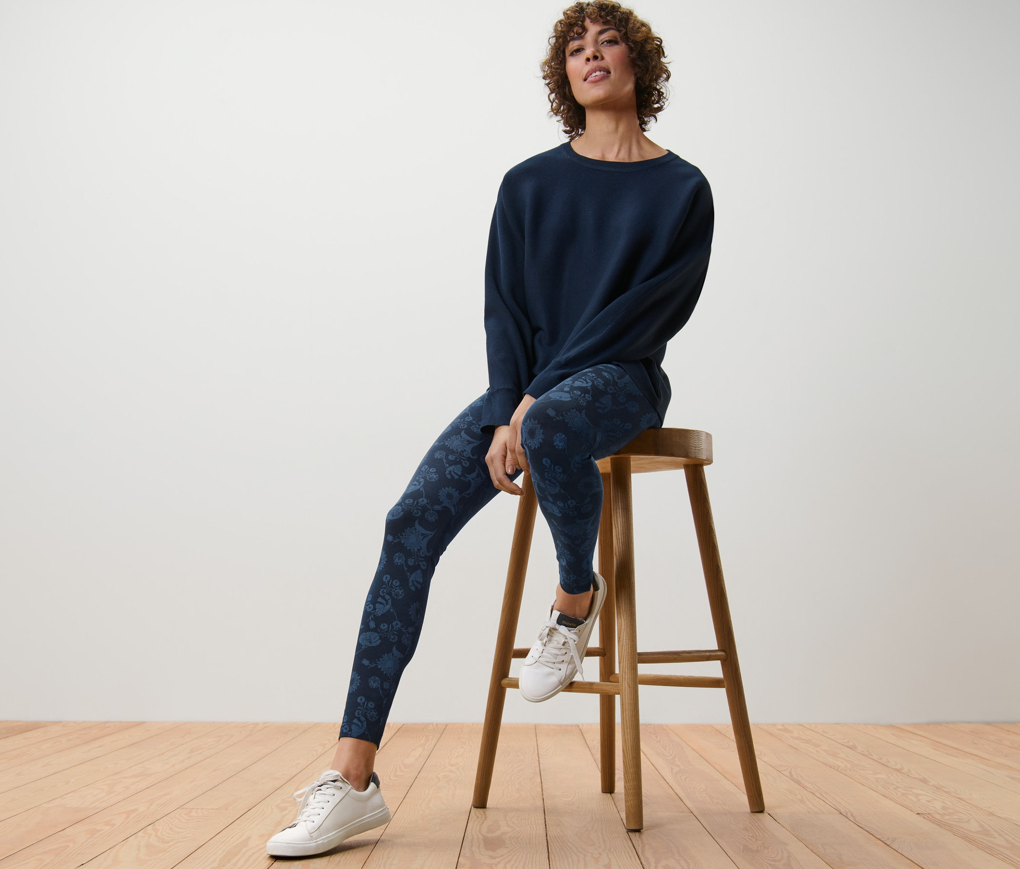 Žena sedí na dřevěné stoličce a má na sobě modré legíny s potiskem.