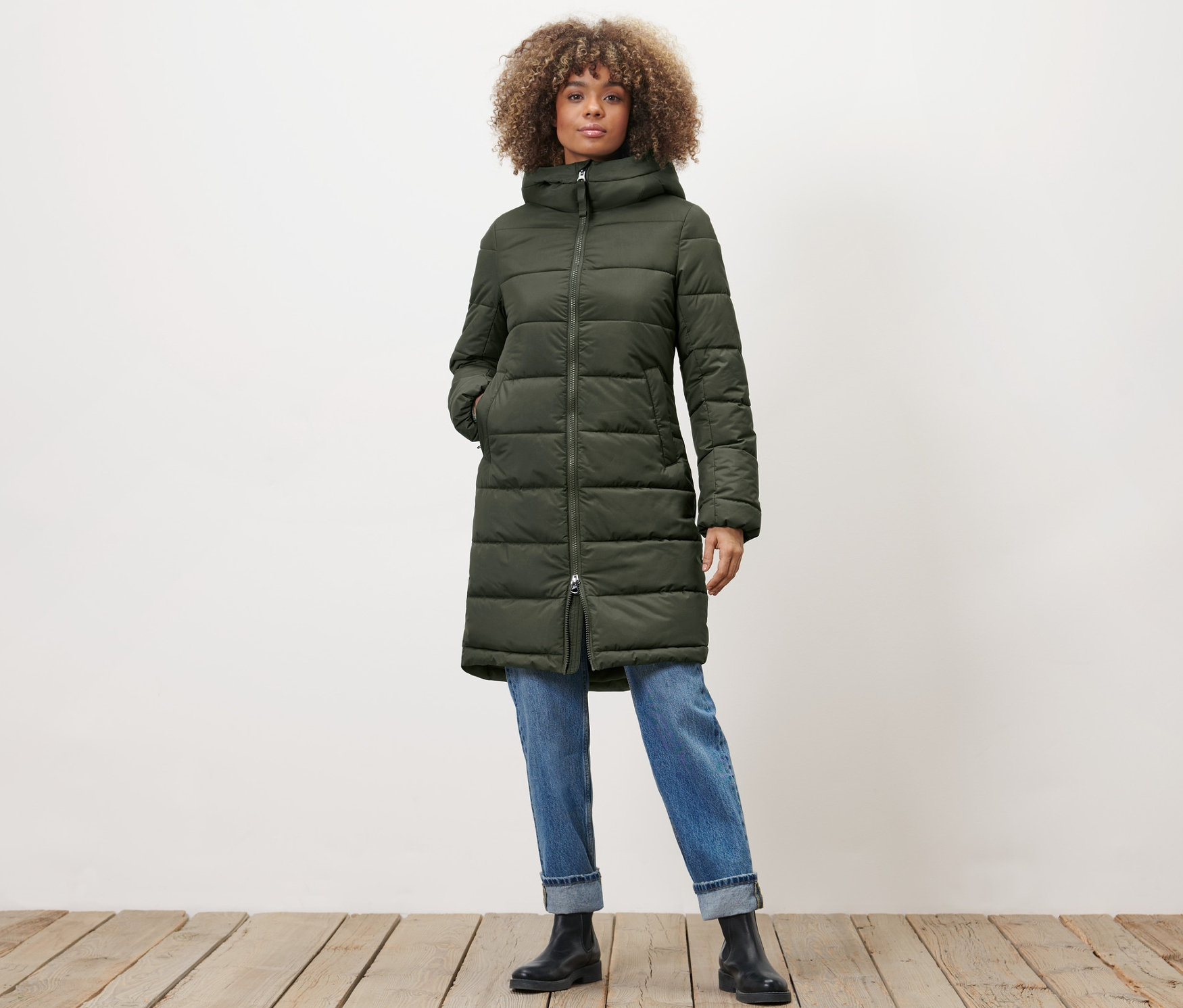 Žena pózuje v khaki prošívaném kabátu.