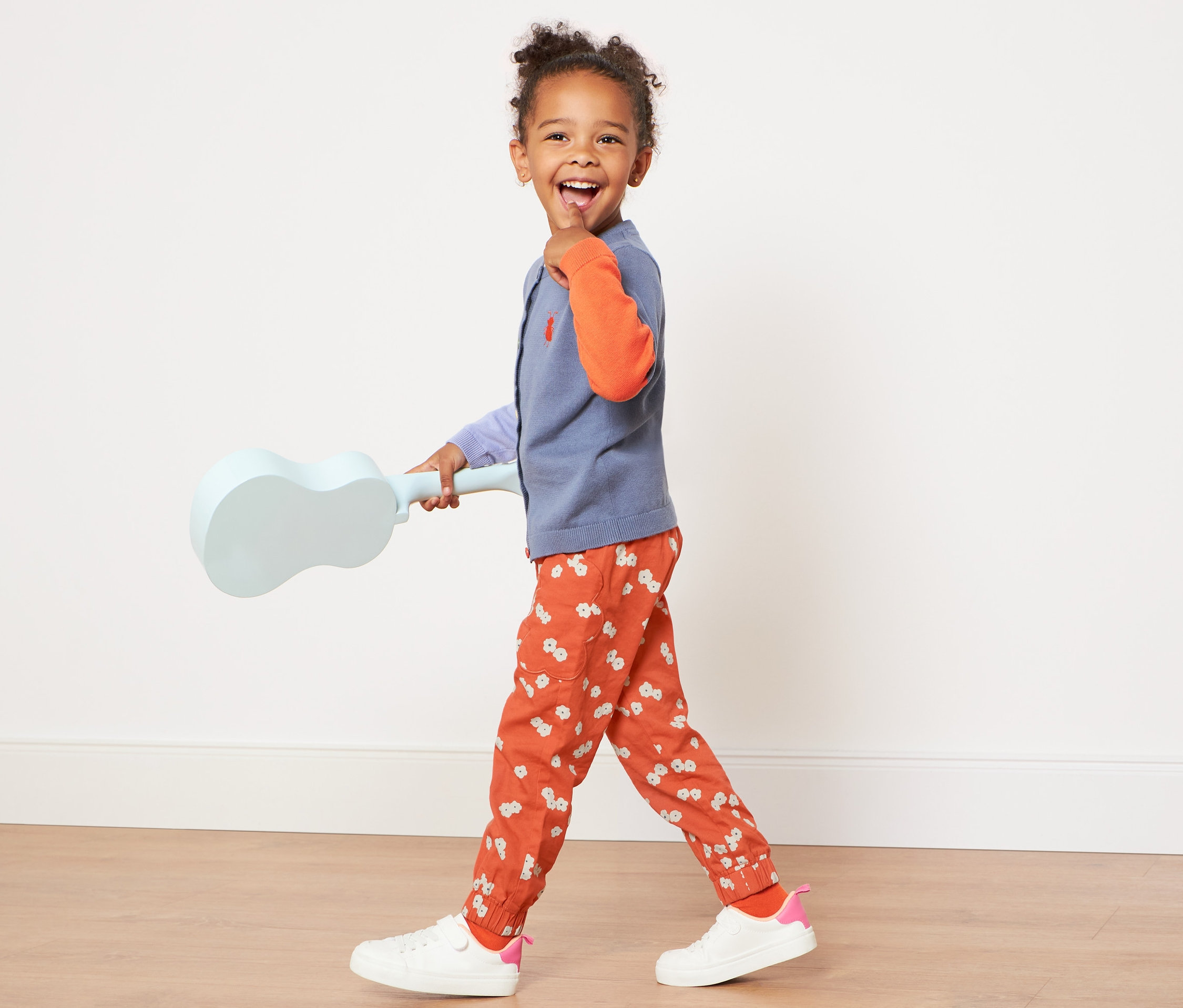 Dívka kráčí a drží ukulele, má na sobě květinové kalhoty pro batolata.