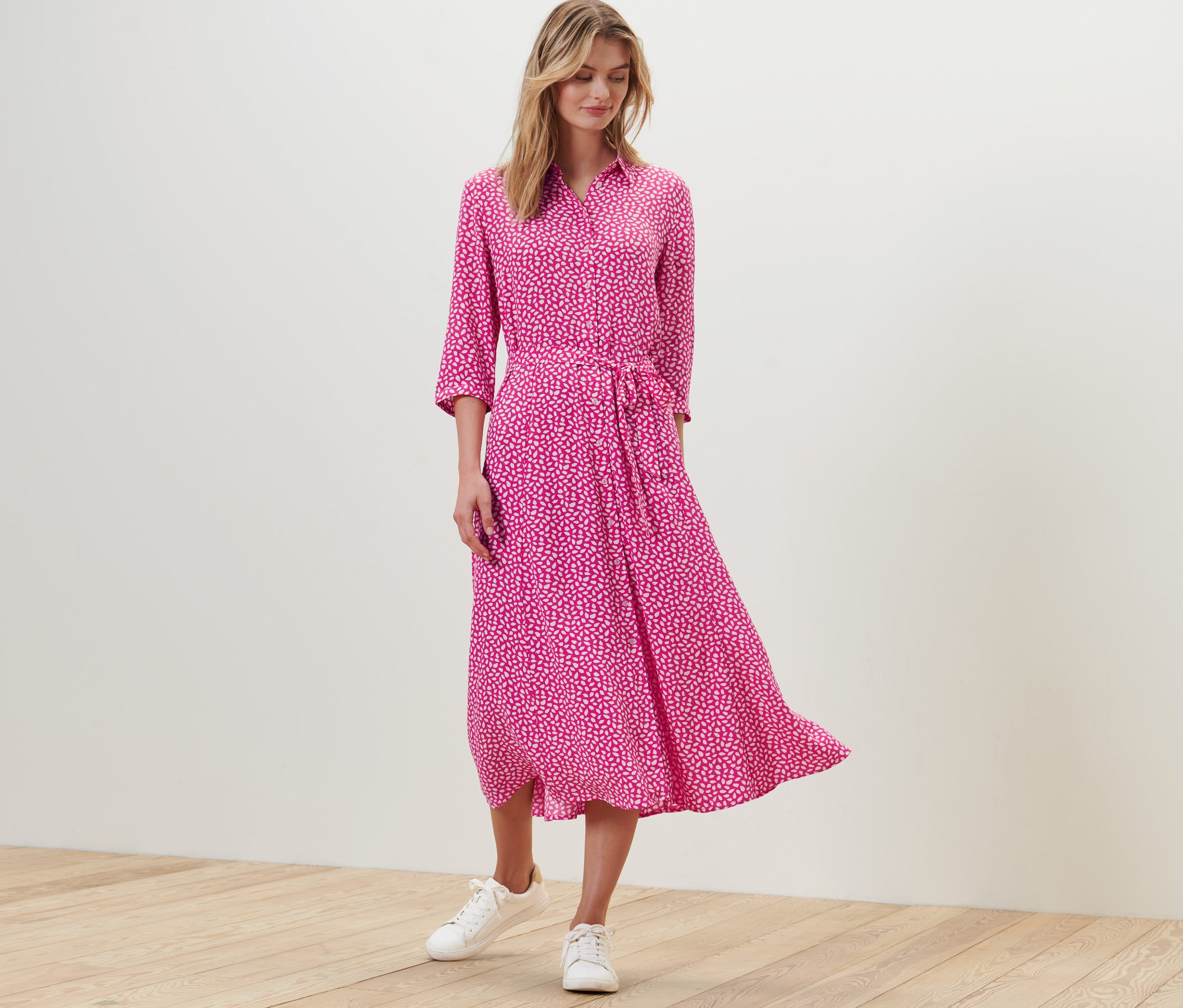 Žena stojí a má na sobě halenkové šaty s potiskem.