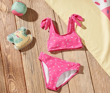 Na dřevěné podlaze leží dětské bikiny, plážová osuška se zmrzlinou a hračky.