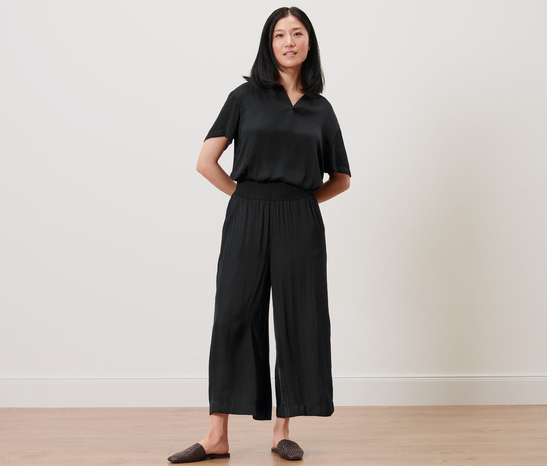 Žena pózuje v černých saténových kalhotách culotte a topu.