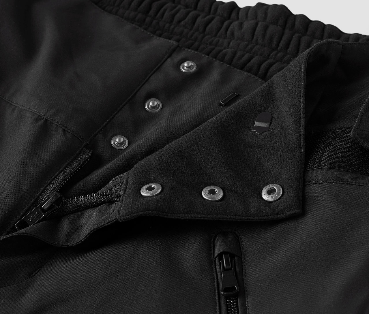 Detail černé látky s knoflíky a zipem.