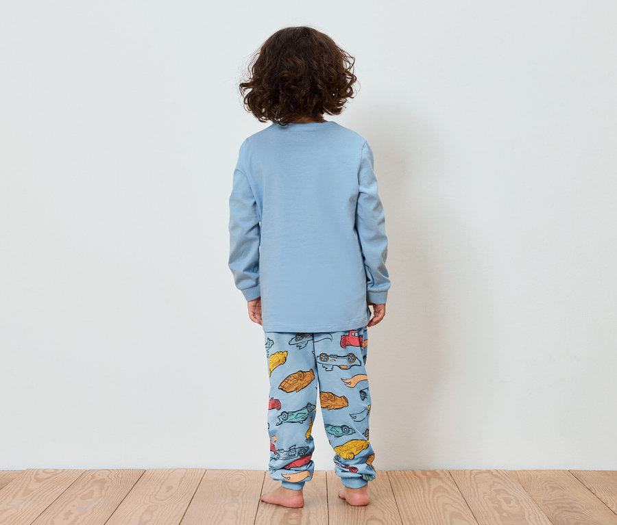 Dítě zády k fotoaparátu má na sobě modré pyžamo s potiskem autíček.