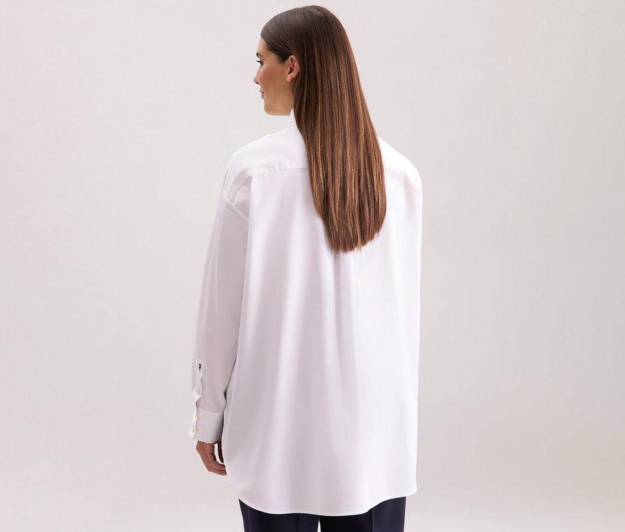 Žena zezadu nosí bílou dlouhou halenku oversize Seidensticker.