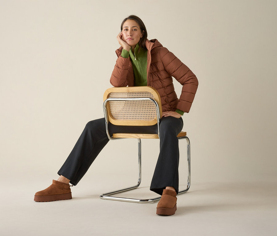 Žena sedí na židli v pleteném svetru troyer, bundě a botách.