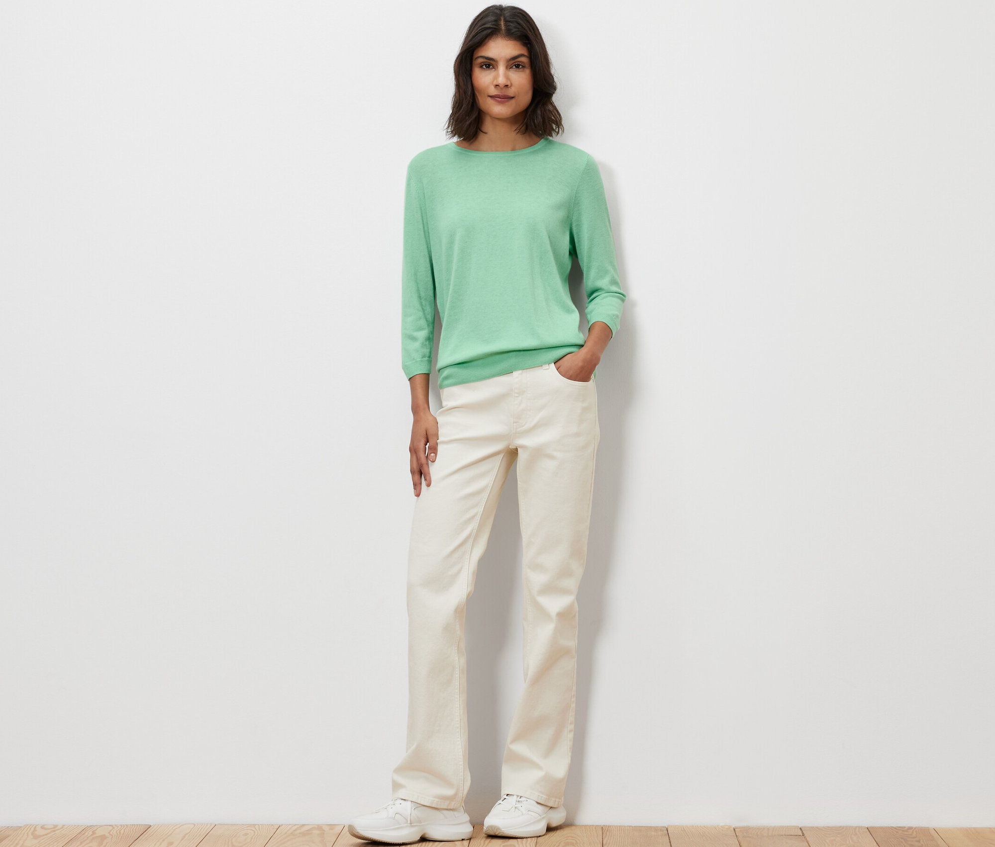 Žena pózuje na sobě světle zelený svetr z jemného úpletu s hedvábím.