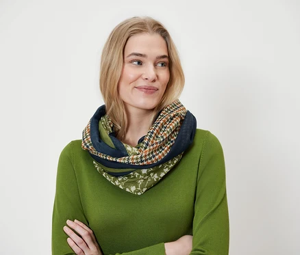 Blonďatá žena nosí vícebarevnou šálu a zelený svetr.
