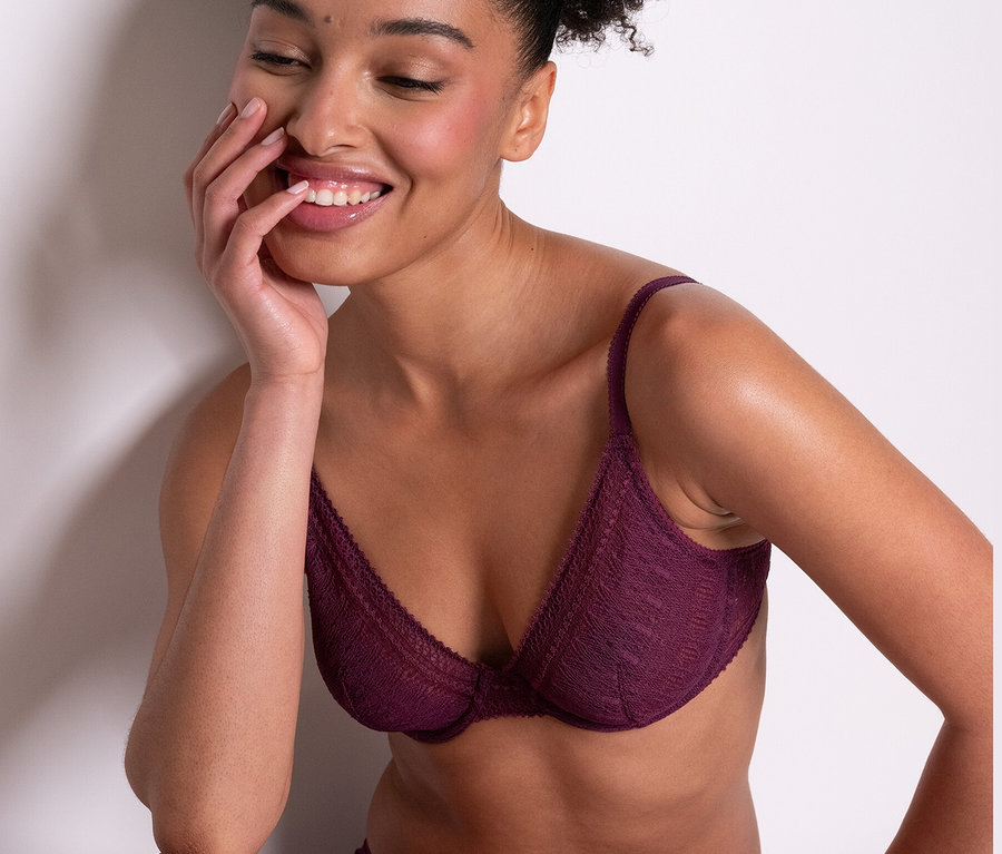Žena sedí a usmívá se, má na sobě fialovou podprsenku s kosticemi Passionata »Leila« a odpovídající kalhotky.