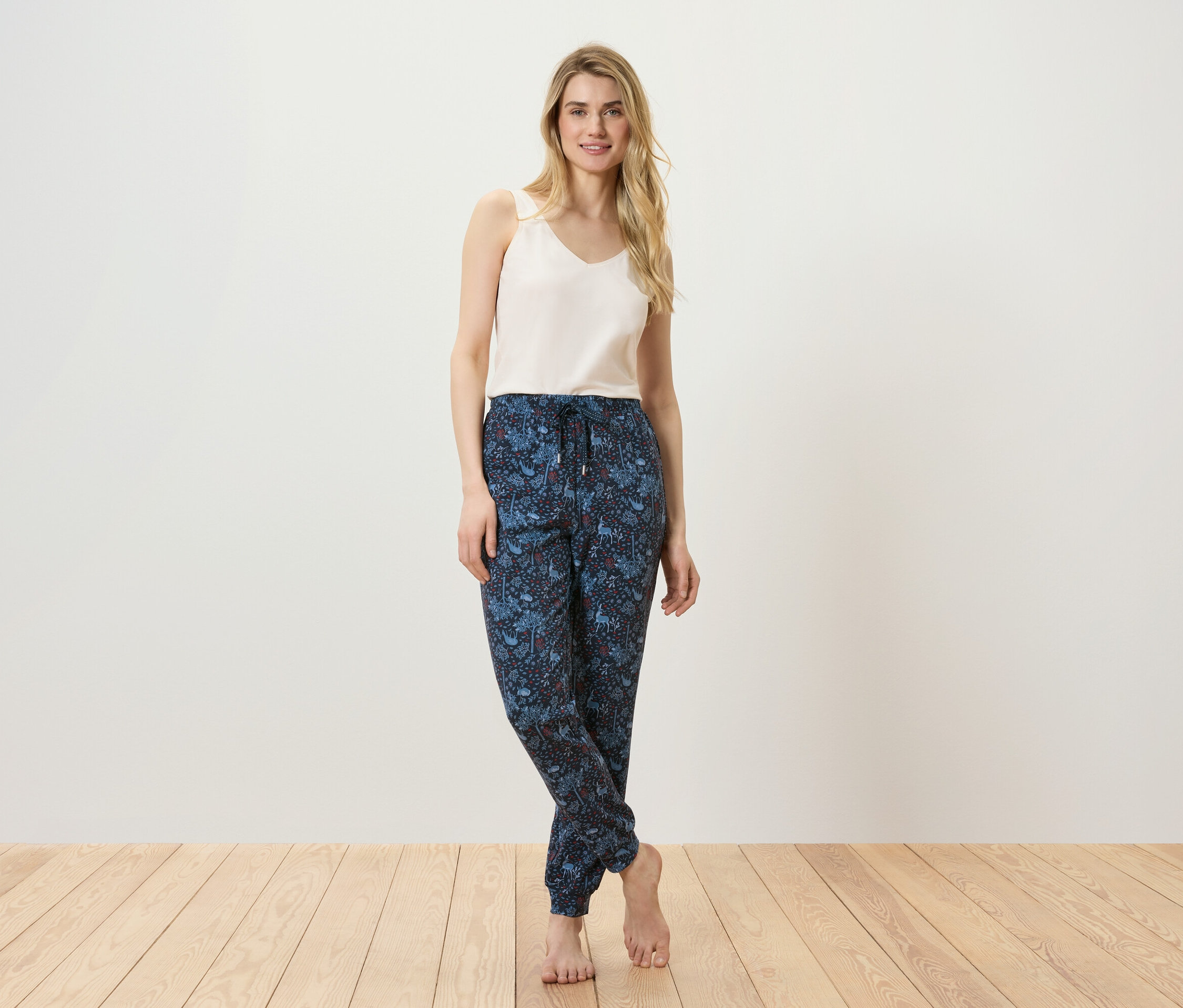 Žena pózuje v tílku a vzorovaných kalhotách na podlaze.