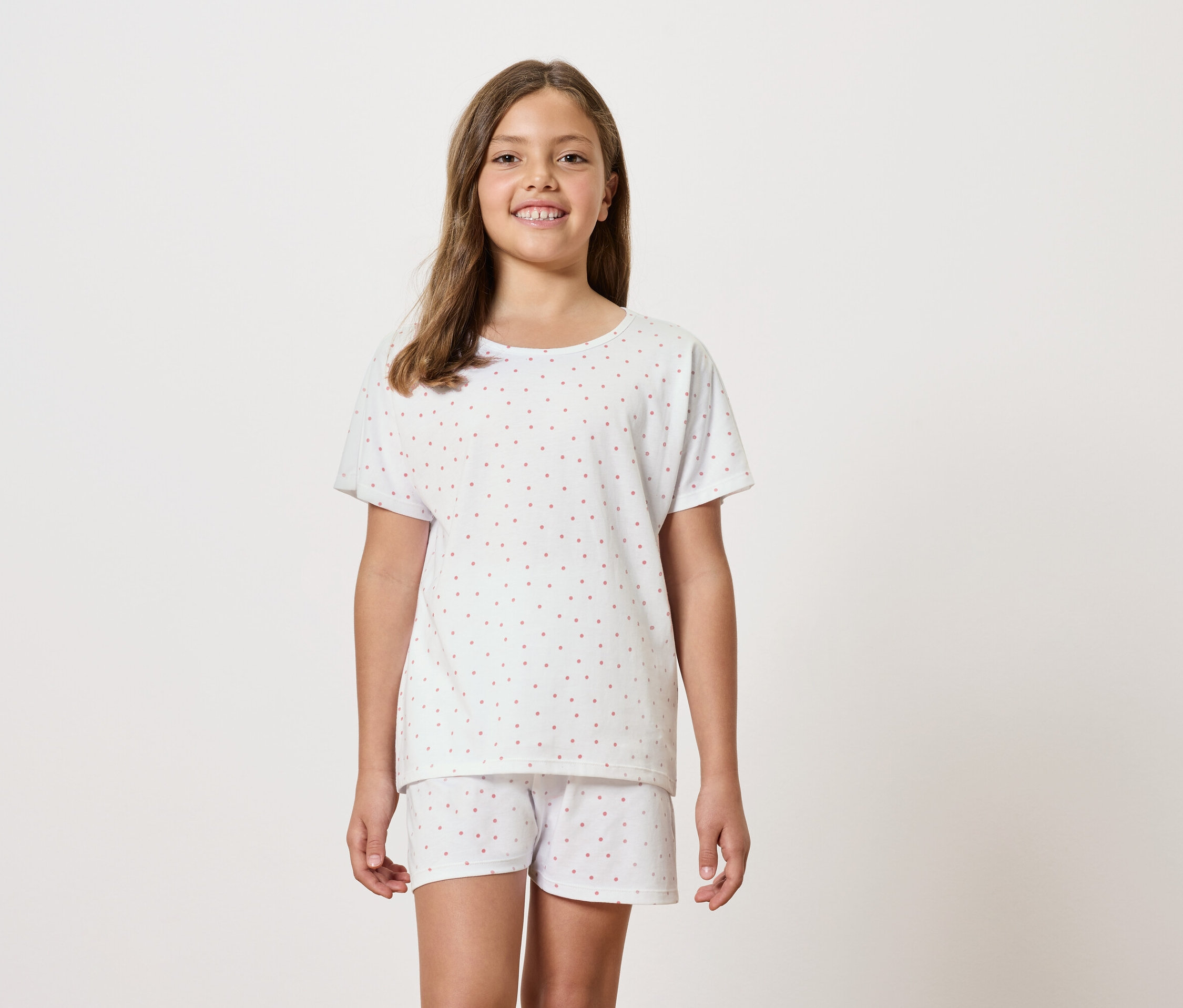 Dívka má na sobě bílé pyžamo s krátkým rukávem a šortkami.