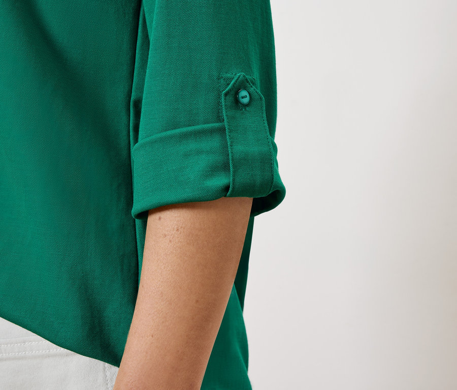 Detail dámské zelené košile s ohrnutými rukávy a knoflíkem.