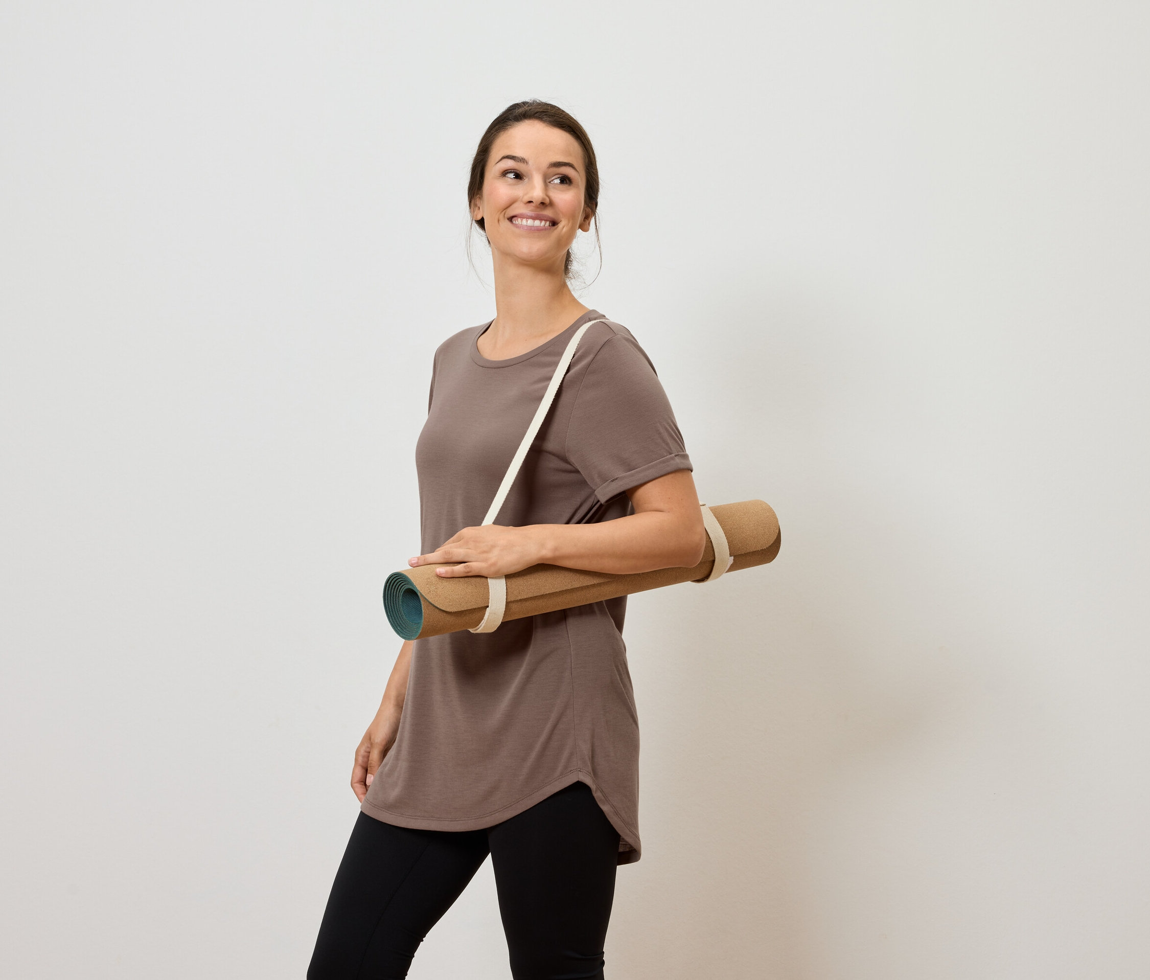 Usmívající se žena nese podložku na jógu přes rameno.