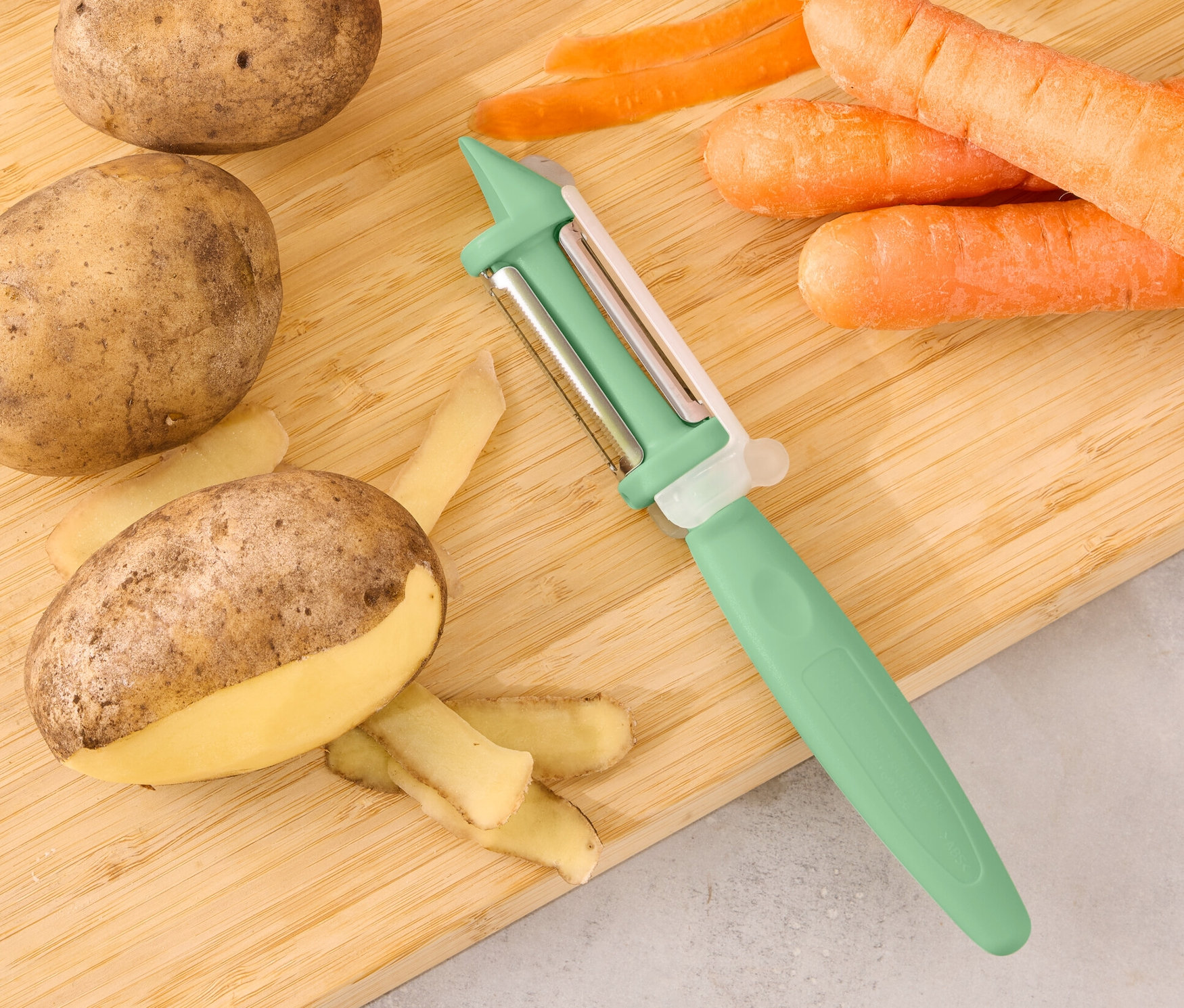 Brambory, rajče, okurka a mrkev leží na prkénku s univerzální škrabkou 2 v 1.