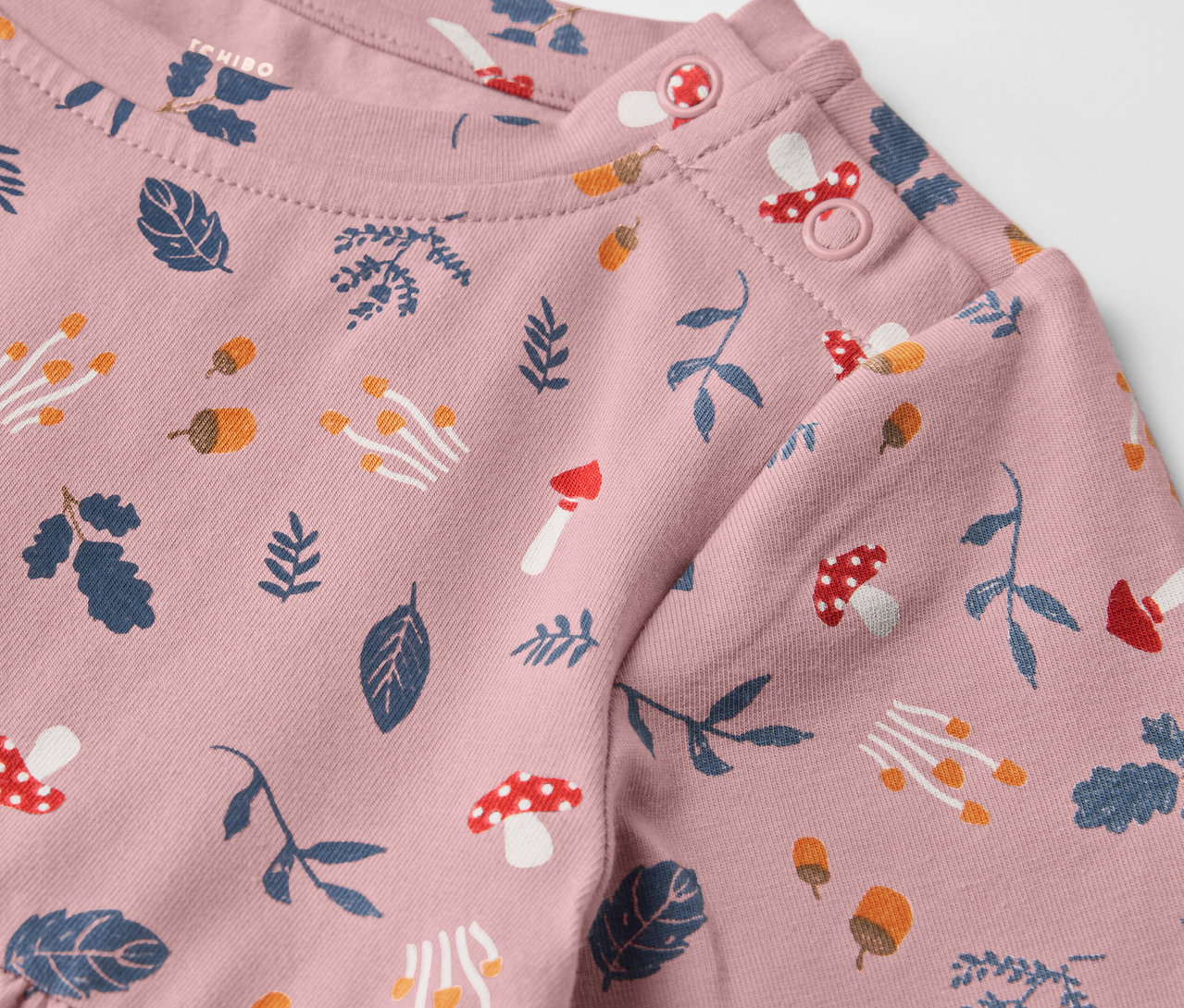 Detail růžových dětských žerzejových šat s potiskem listů a hub.