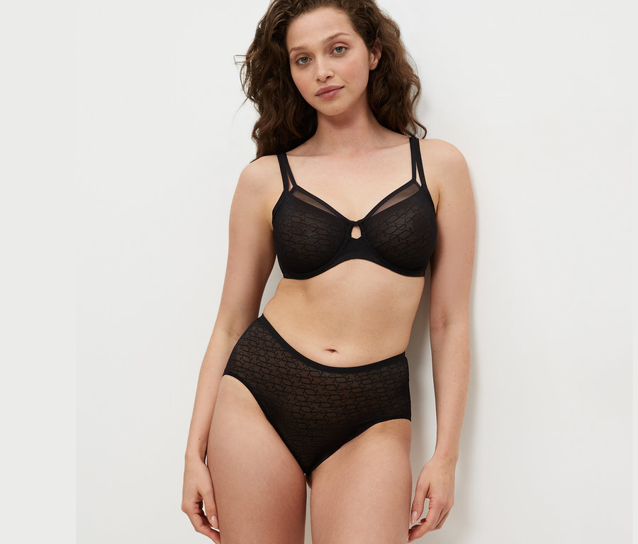 Žena má na sobě černou zmenšující podprsenku Triumph Signature Sheer a černé kalhotky.