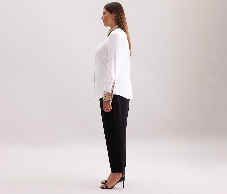 Žena stojí bokem a má na sobě bílou popelínovou halenku Seidensticker s kostkovaným detailem, černé kalhoty a černé boty na vysokém podpatku.