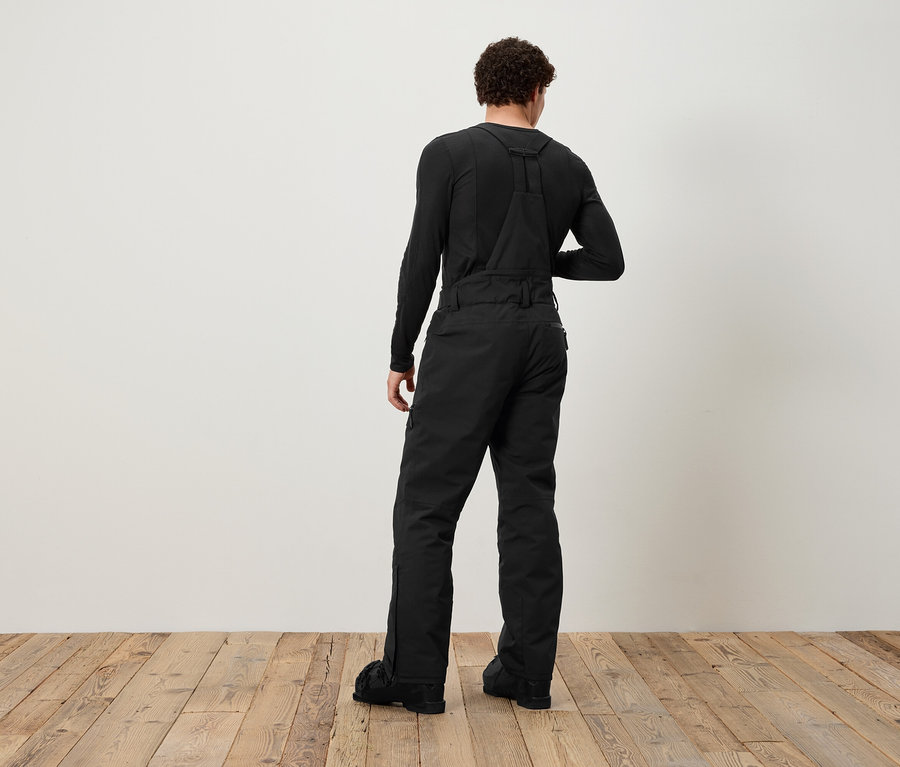 Muž zády ke kameře má na sobě černé lacláče a černé tričko s dlouhým rukávem.