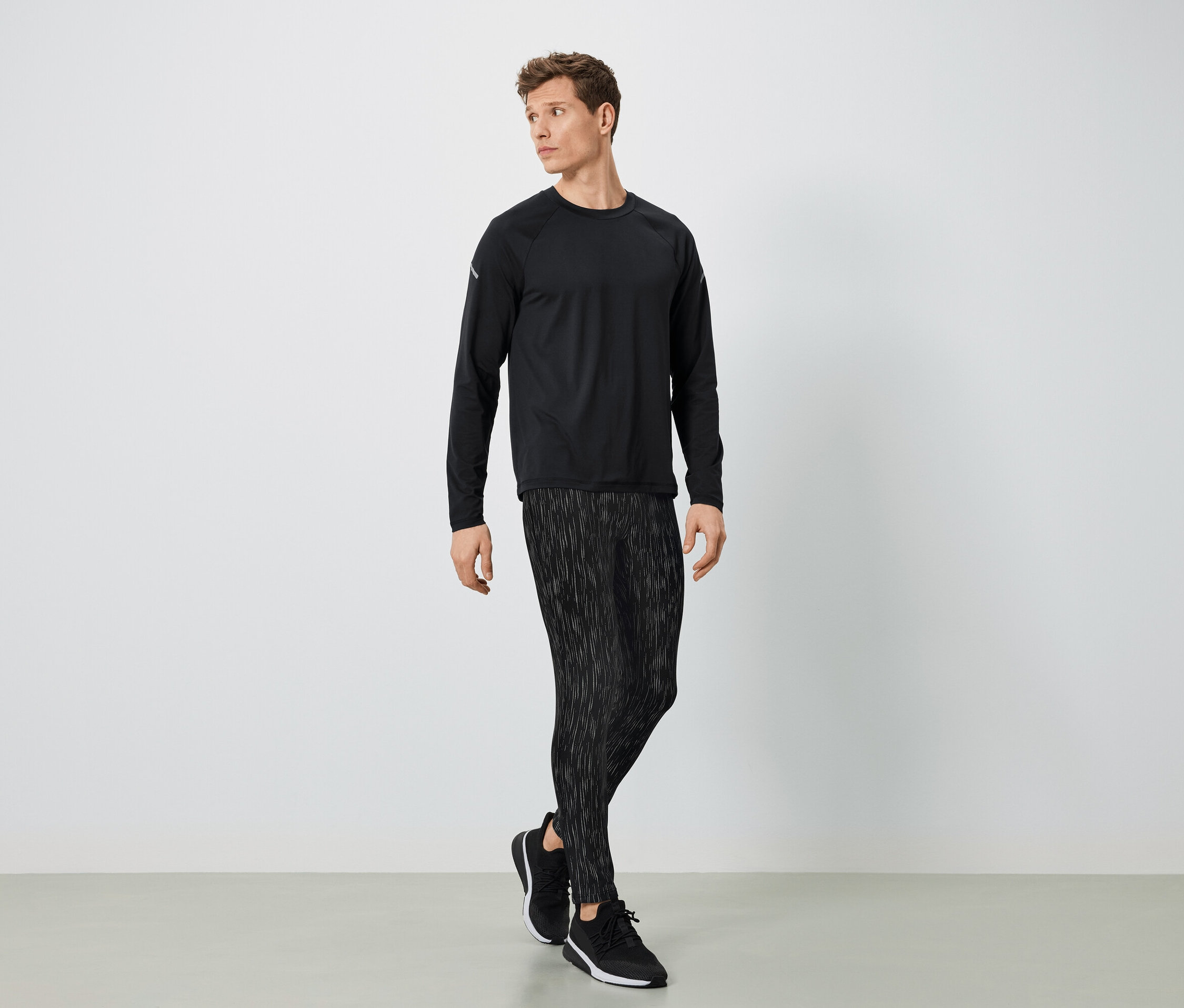 Muž v černém sportovním oblečení pózuje na světlém pozadí.