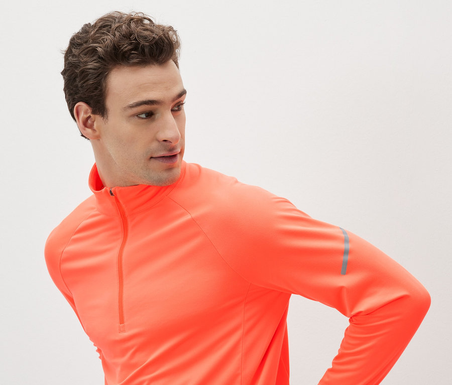 Muž v oranžovém sportovním tričku s dlouhým rukávem a zipem.