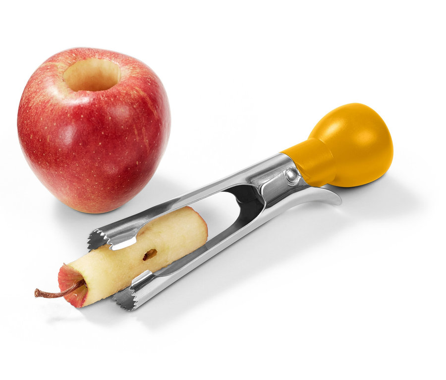 Červené jablko s vydlabaným středem stojí vedle nerezového odstraňovače jadřinců s žlutou rukojetí, který odstraňuje jádřinec z druhého jablka.