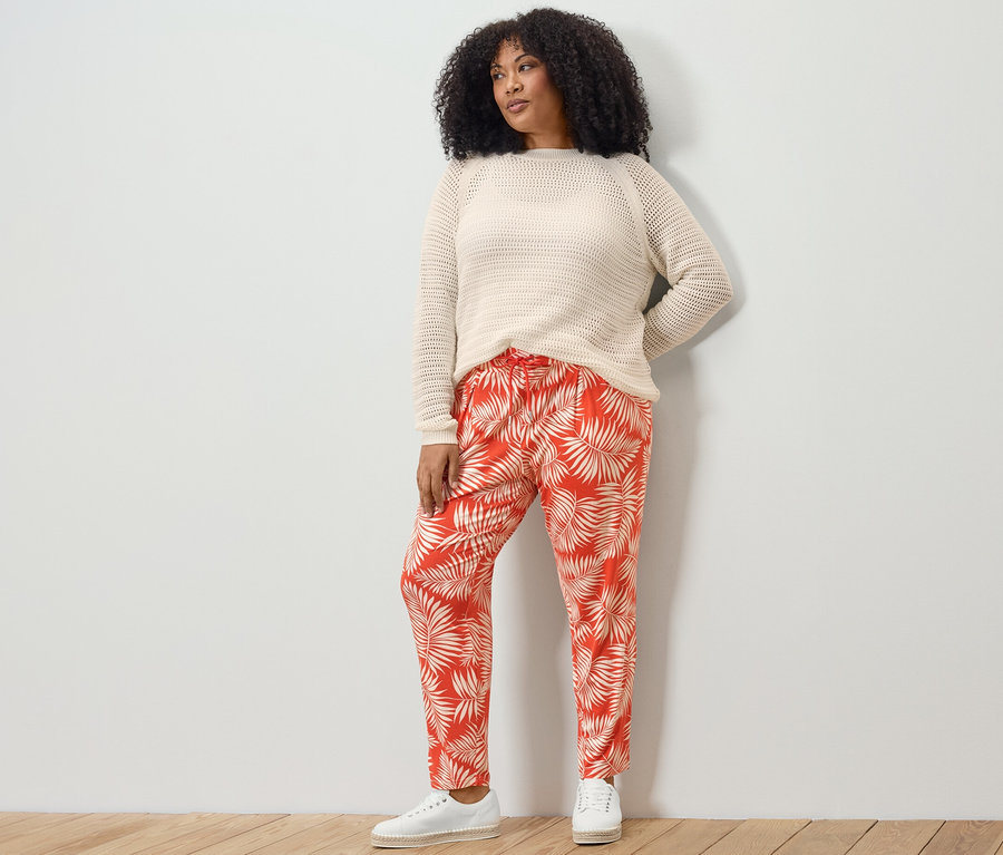 Žena pózuje na sobě svetr z úpletu pointelle a žerzejové kalhoty s potiskem.