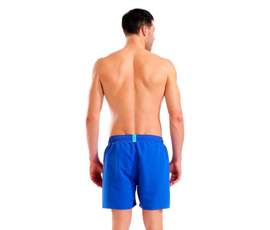 Pohled zezadu na muže v modrých plavkách na bílém pozadí.