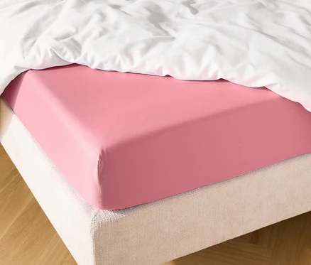 Detailní záběr postele s růžovým prostěradlem a bílou přikrývkou.