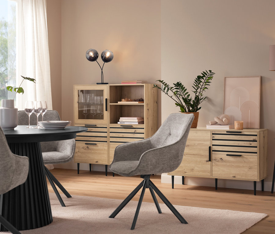 Jídelna s kulatým stolem, šedými židlemi, vitrínou »BAAKEN« se skleněnými dvířky, regálem »BAAKEN« se zásuvkami a sideboardem se zásuvkami.